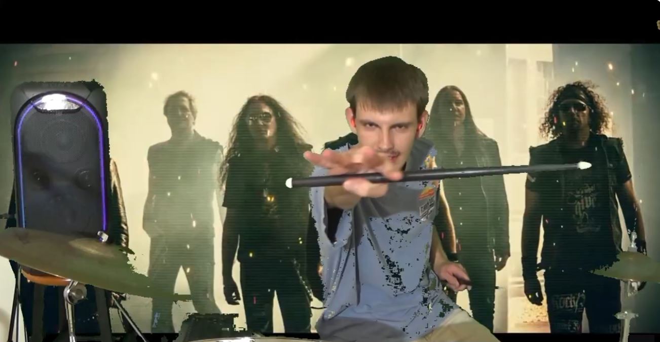 Carter seated at a drum kit, holding a drumstick toward the camera, with a rock music backdrop.